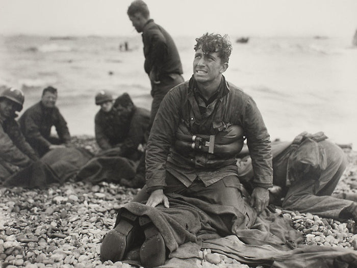 Black-and-white photograph of exhausted soldiers on Omaha Beach after the D-Day landings, 6 June 1944