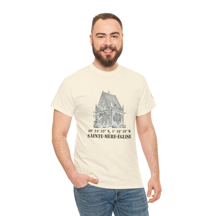 Cream t-shirt with Sainte-Mère-Église graphic by Veteran owned, featuring building illustration and coordinates, worn with blue jeans.