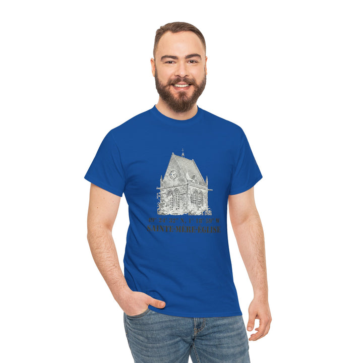 Blue Sainte-Mère-Église church t-shirt by Veteran owned, featuring a building graphic, worn with jeans by a smiling model.