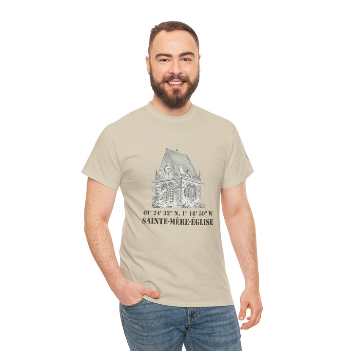 Sand-colored t-shirt by Veteran owned, featuring a Sainte-Mère-Église vintage church drawing and lettering, styled with jeans.
