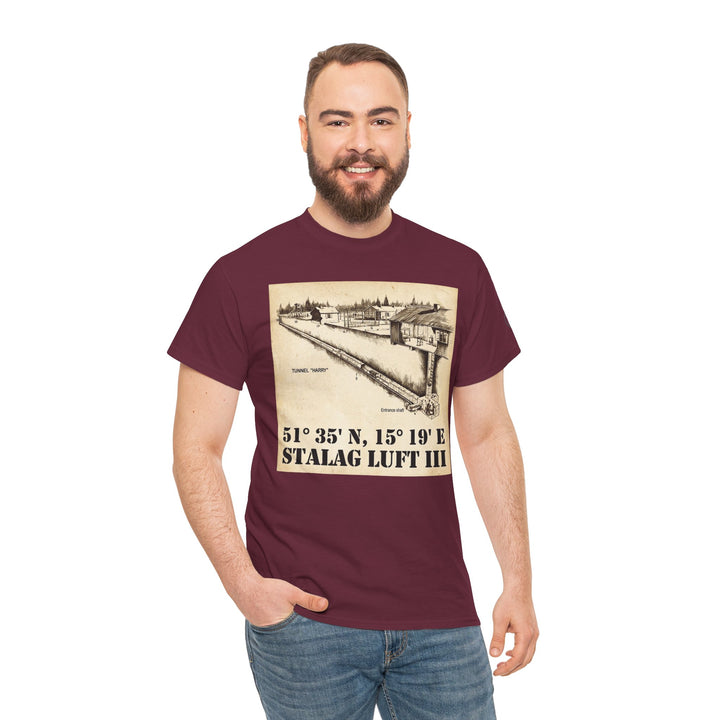 Maroon graphic t-shirt by Veteran owned, featuring Stalag Luft III coordinates and a vintage-style illustration. Man wears blue jeans.
