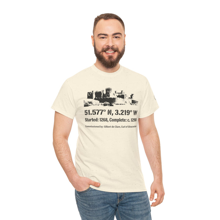 Cream-colored T-shirt by S&amp;W Gallus featuring a graphic of Caerphilly Castle and coordinates, worn with jeans by a smiling man.
