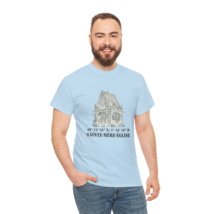 Light blue t-shirt by Veteran owned, featuring a vintage church graphic and Sainte-Mère-Église coordinates. The man is wearing jeans.