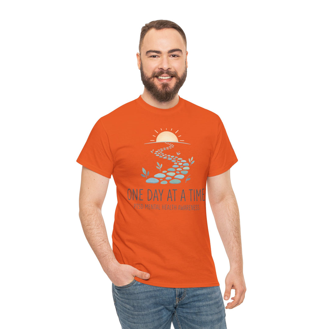 Orange t-shirt by Veteran owned, featuring a pathway, sun, and text design, worn with blue jeans.